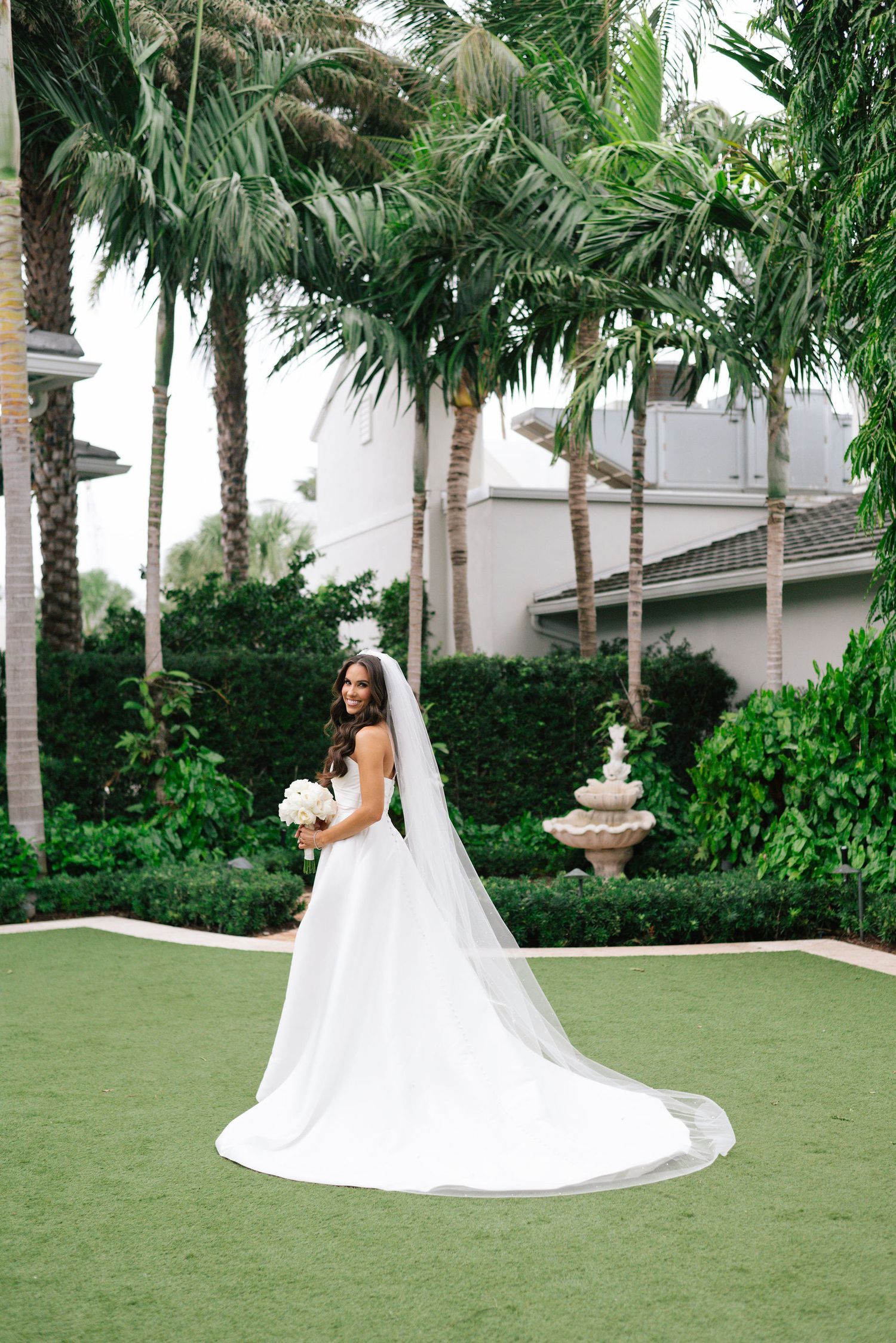 Flowing white wedding gown photographed on lawn with tropical palm trees.
