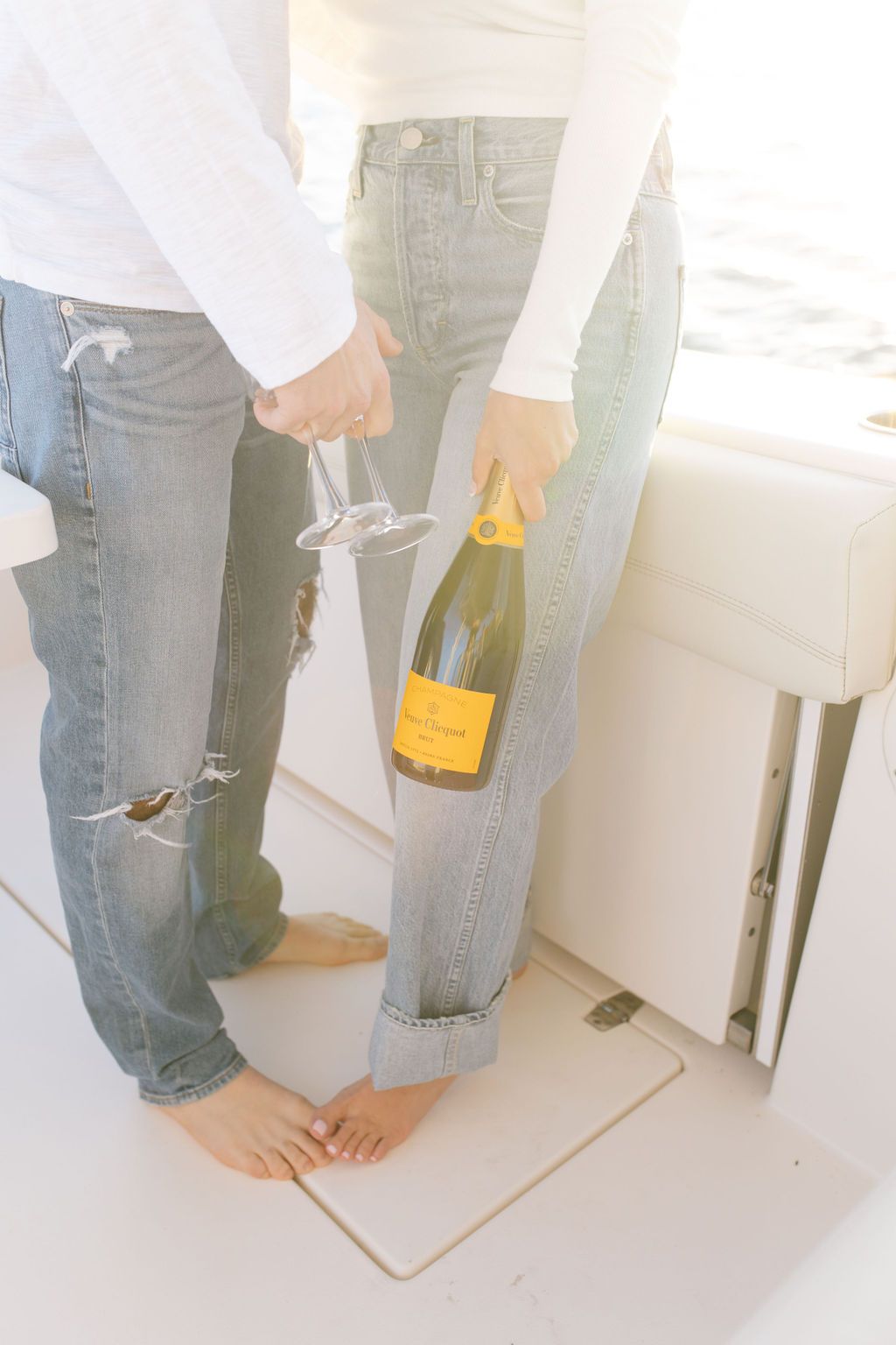 Close-up of distressed denim jeans and casual footwear on white boat deck.