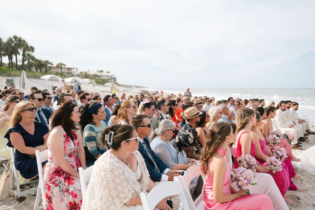 Wedding guests seated in rows on the beach for an oceanfront ceremony.