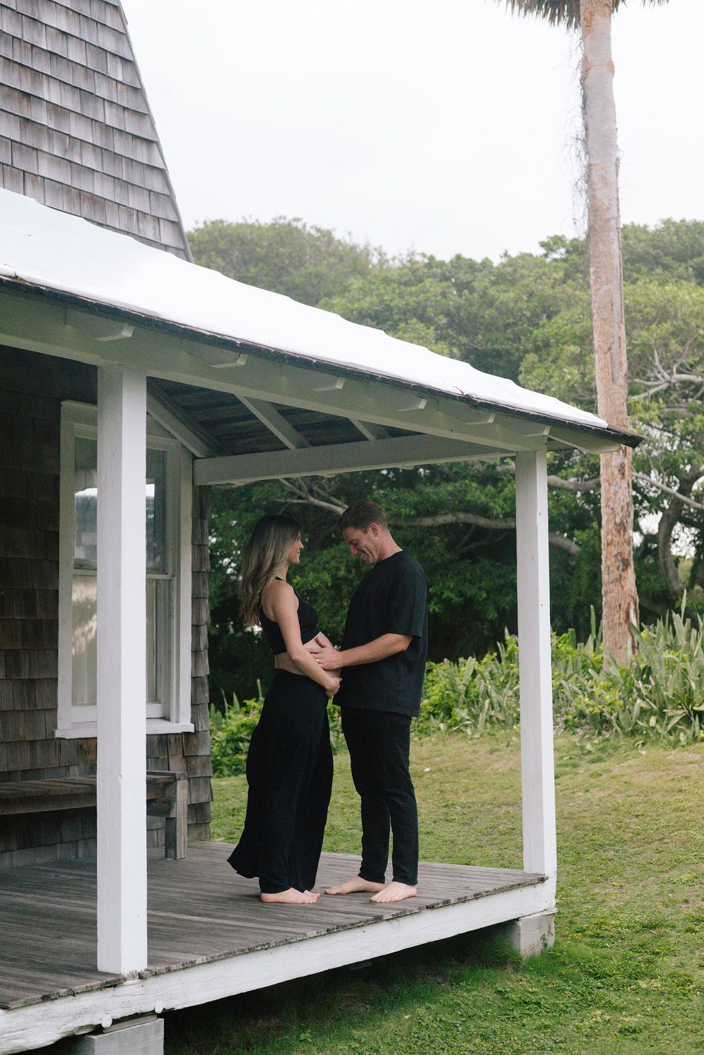 A couple shares intimate moments on a white porch with palm trees in the background.