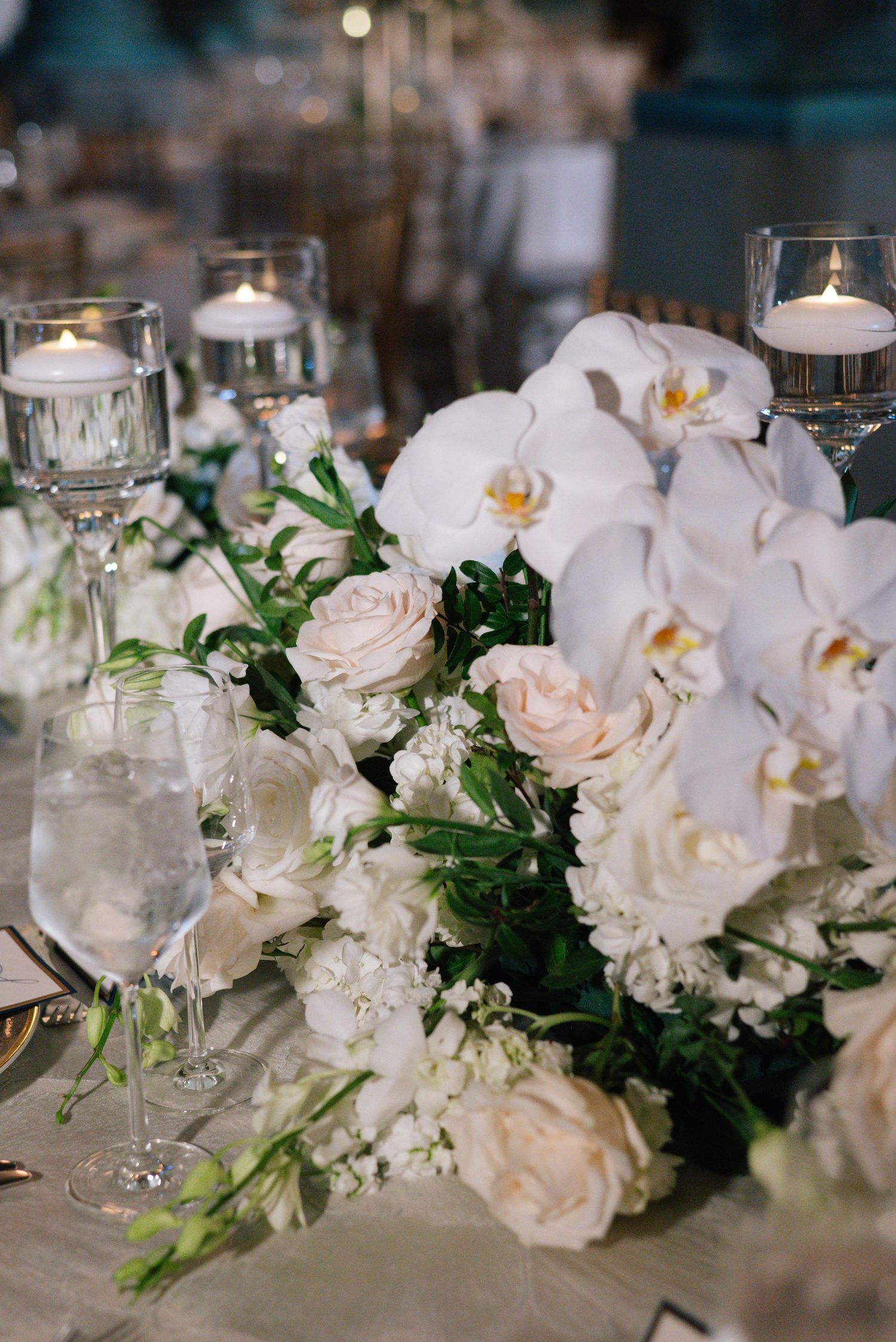 White orchids, blush roses, and floating candles create a romantic wedding table centerpiece.
