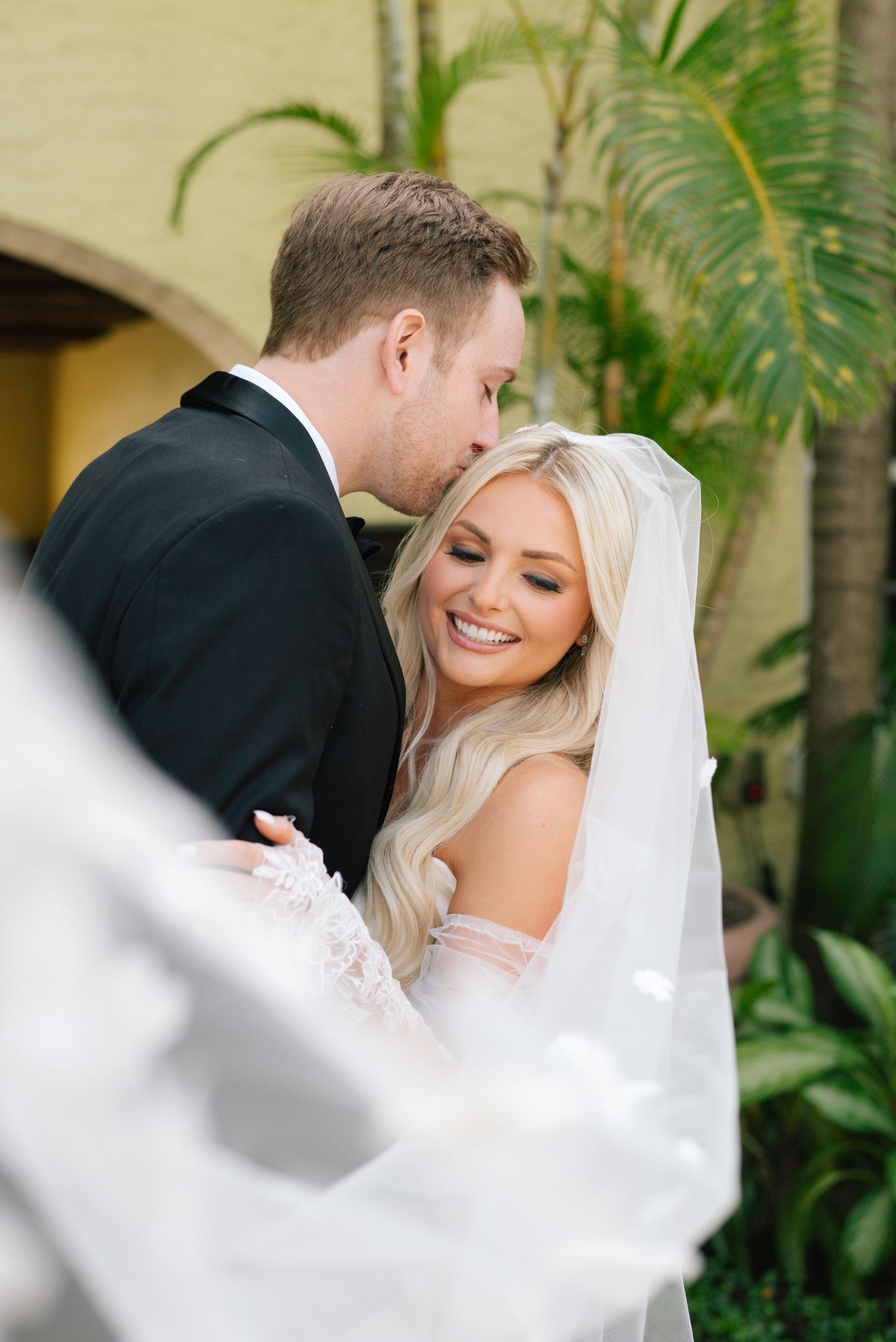 A romantic wedding moment captured outdoors with palm trees in the background.