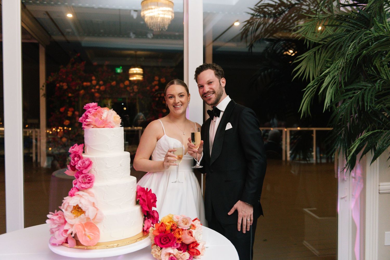 Wedding reception venue with white tiered cake decorated with pink and coral flowers.