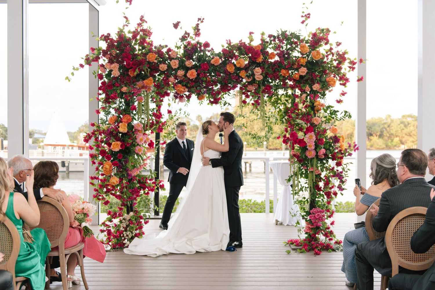 An elegant outdoor wedding ceremony under a floral-adorned white pergola.