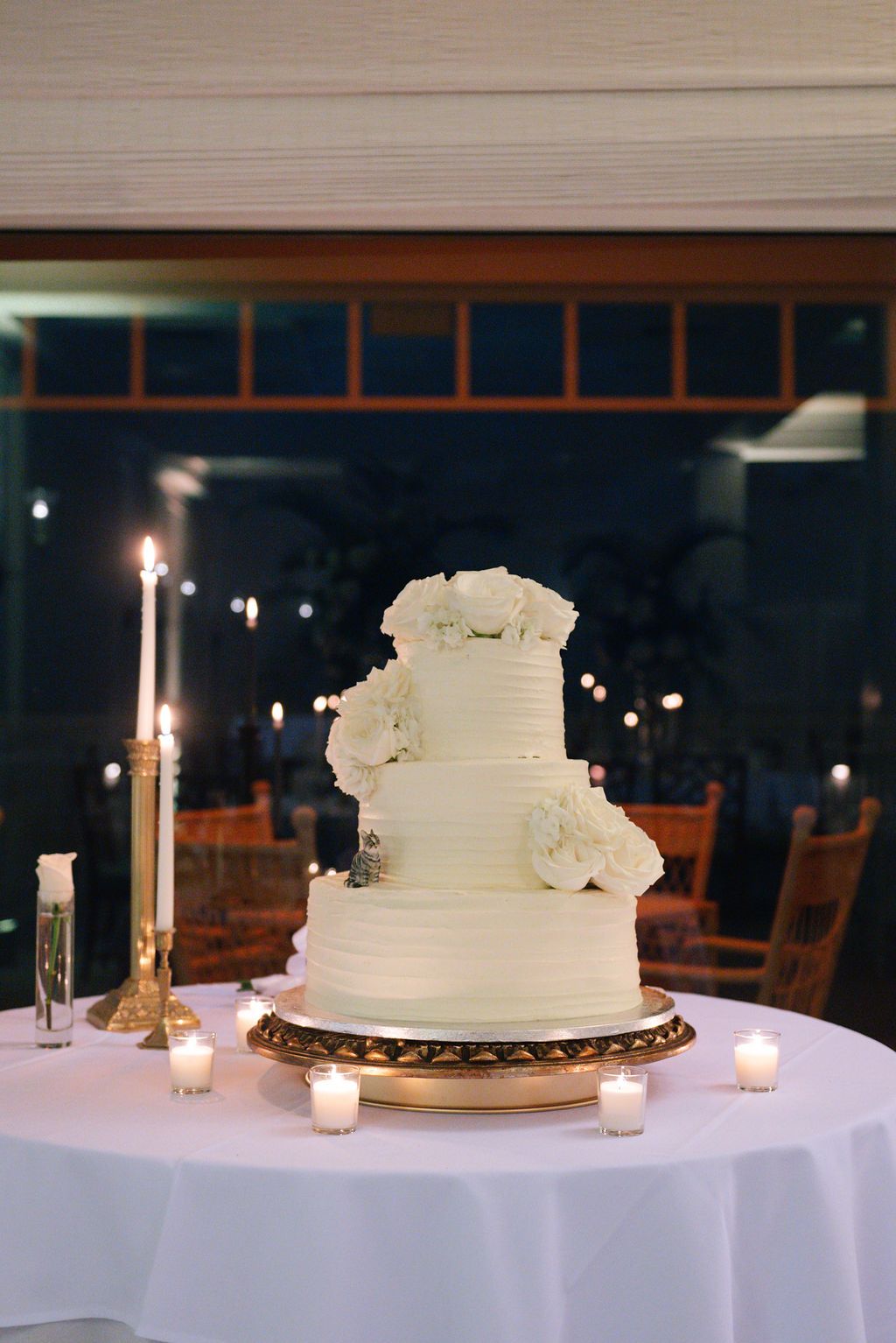 White wedding cake decorated with roses and surrounded by glowing candles on an elegant table setting.
