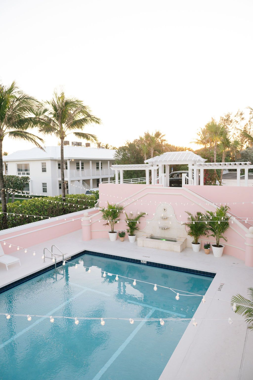 Pink resort building with string-lit pool area and palm trees at dusk.