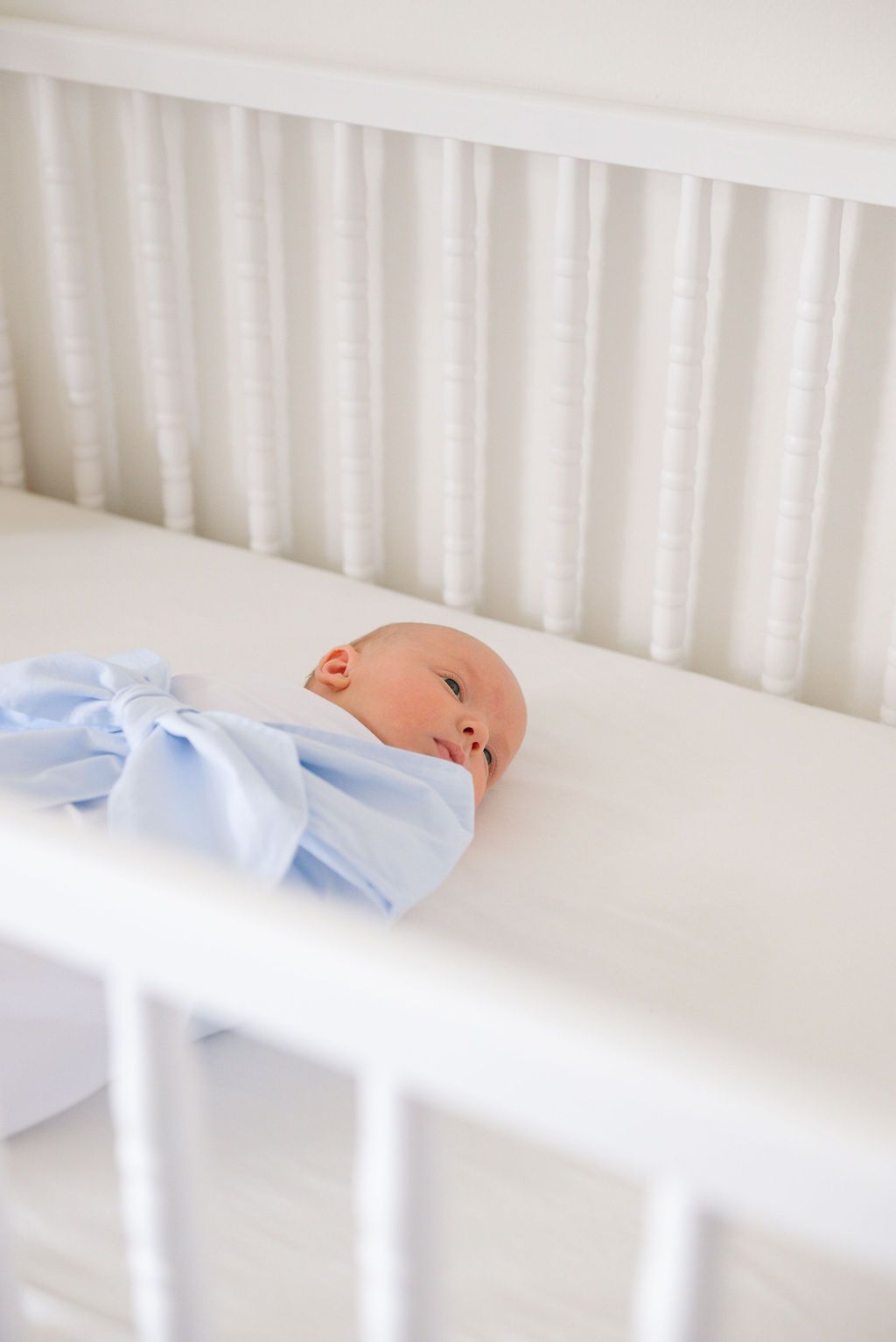 Baby lying in white crib wearing light blue and white outfit.