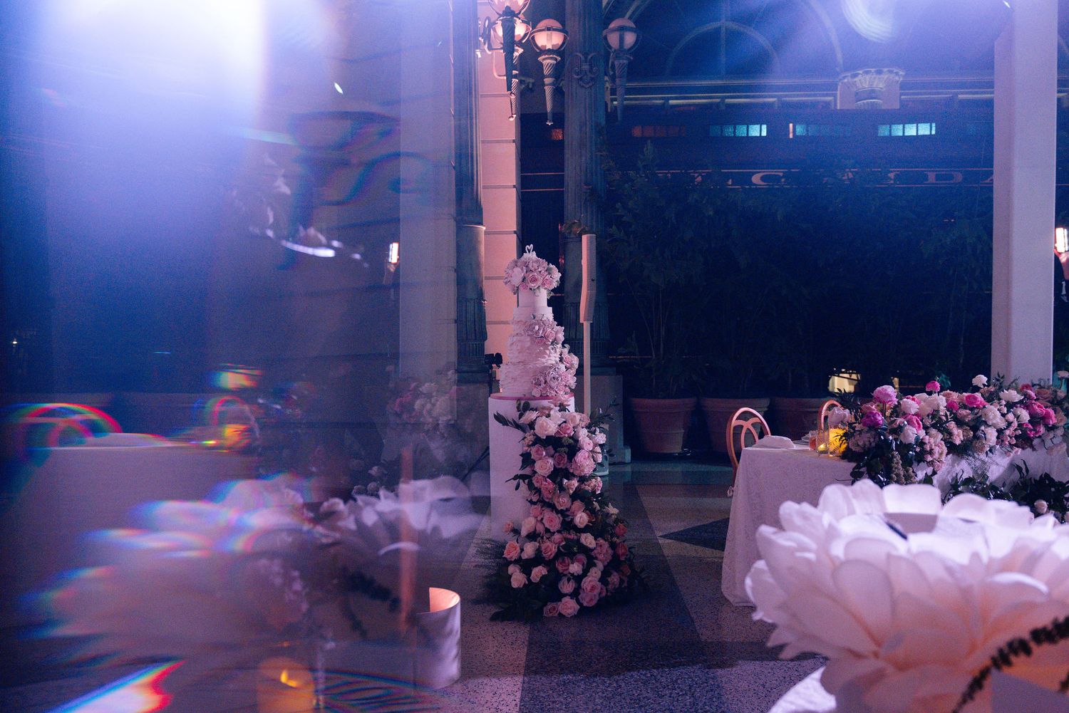 Dramatic blue-lit event space with floral decorations and elegant table settings.