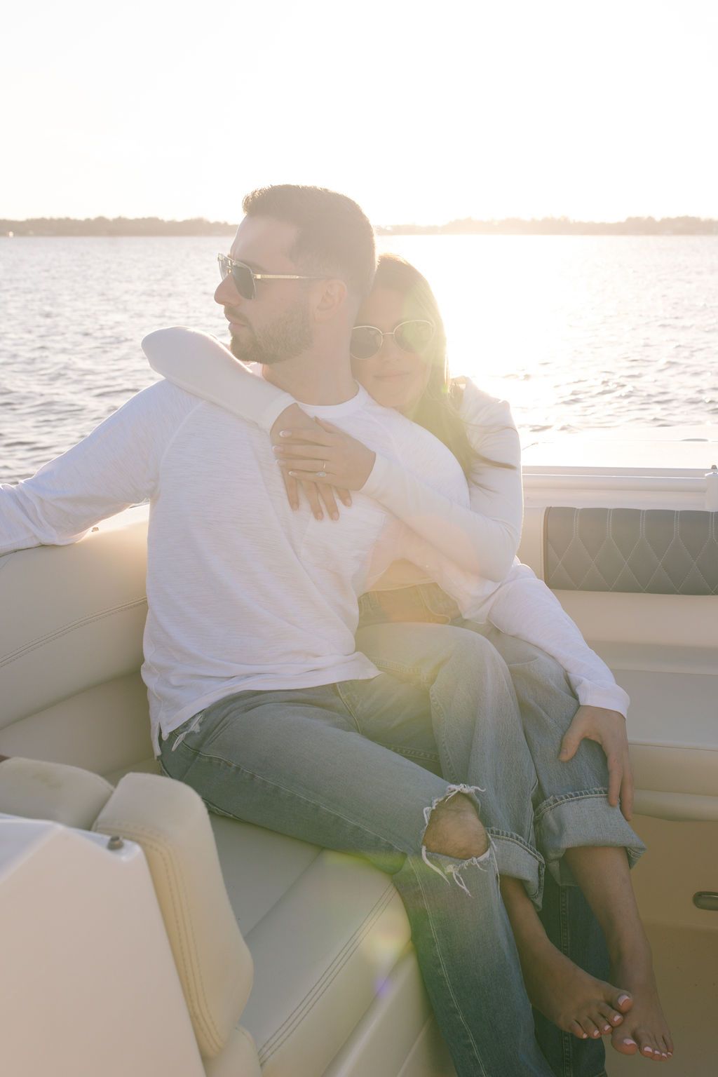 Intimate moment between couple cuddling on boat cushions with sunlight streaming across the water.