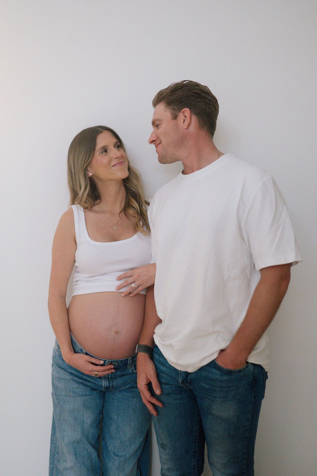 An expectant couple shares intimate moments while wearing casual denim and white tops.