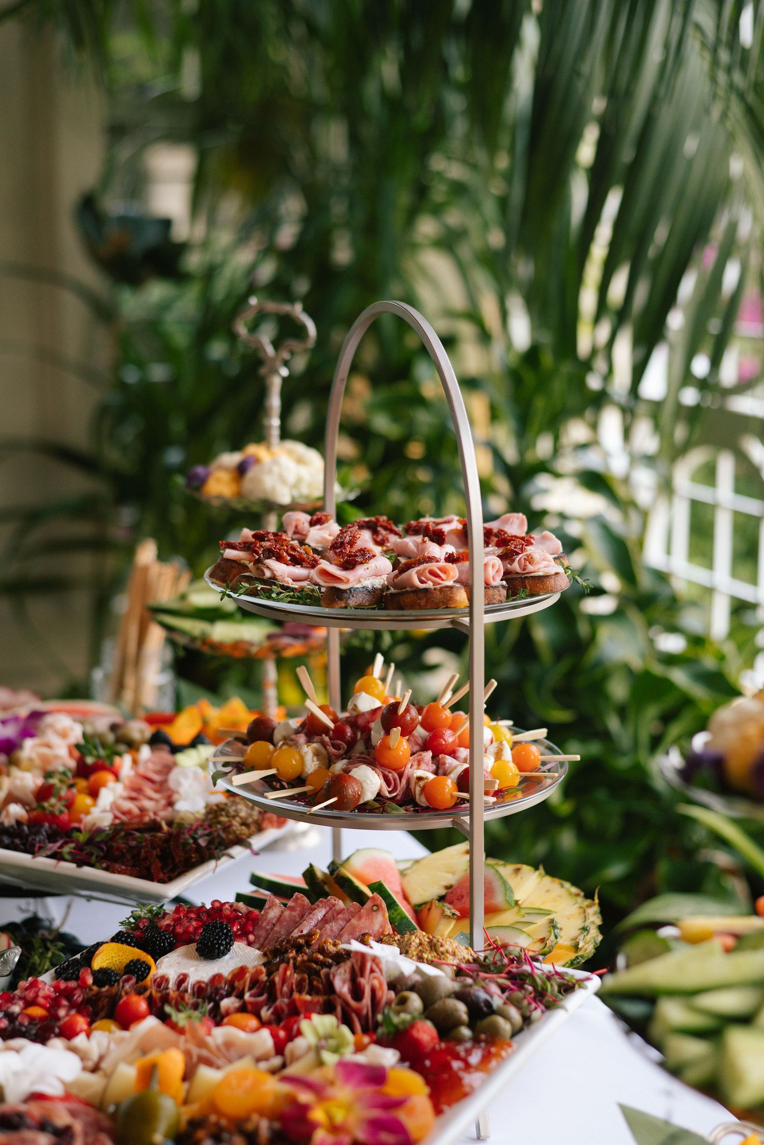 Gourmet food display featuring colorful fruits, meats and appetizers on white tablecloth.