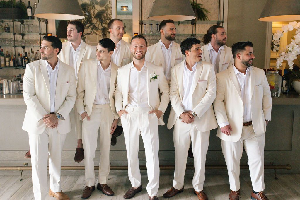 Groomsmen in all-white suits walking in formation indoors.