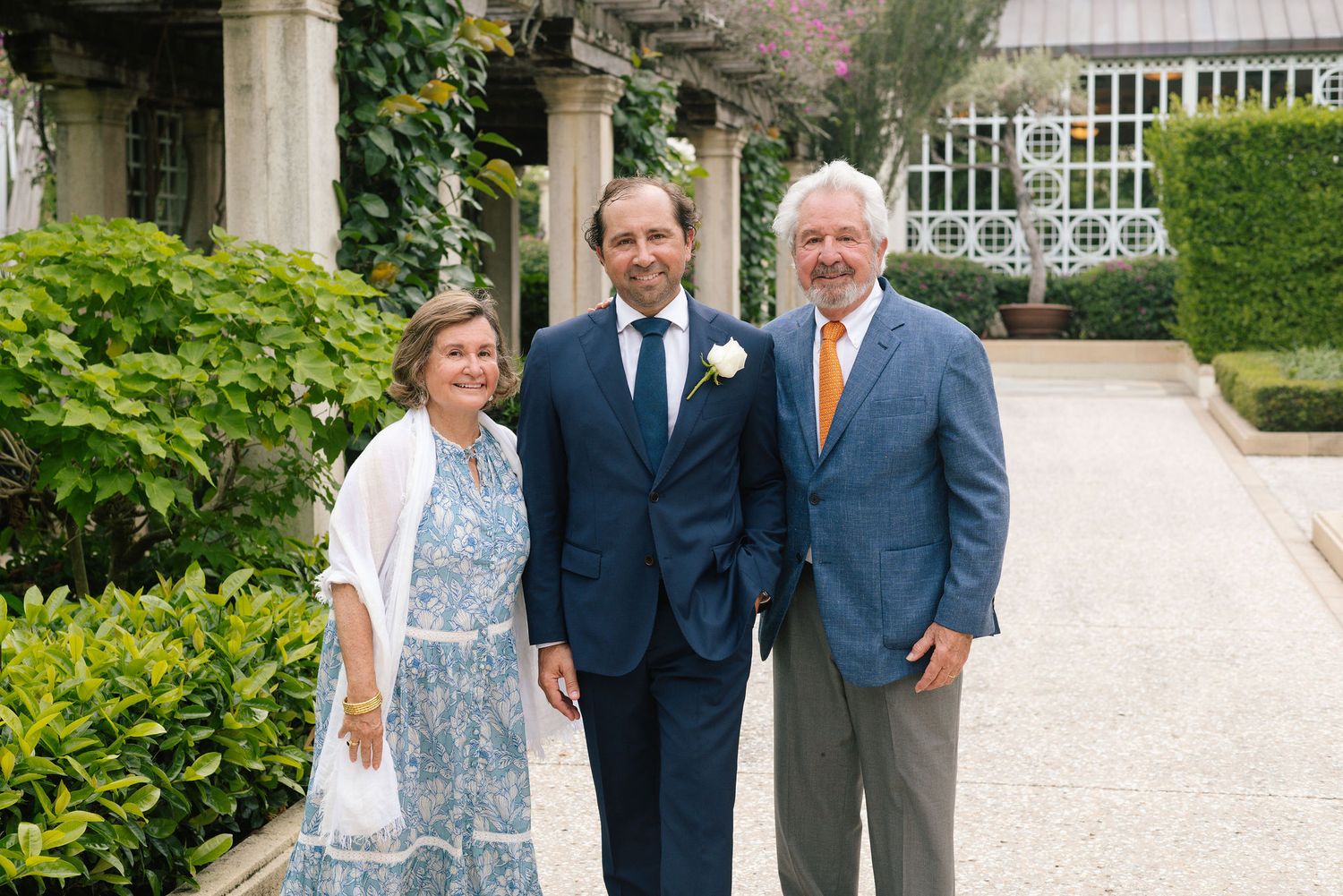 Wedding guests gather on elegant stone walkway near tropical garden and ornate greenhouse.