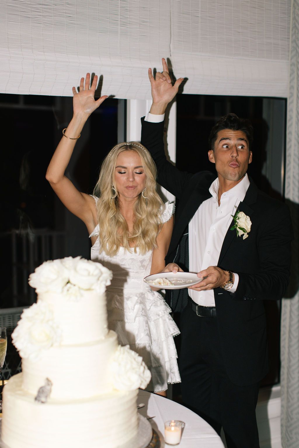 Wedding party members raise their hands in celebration near the wedding cake.