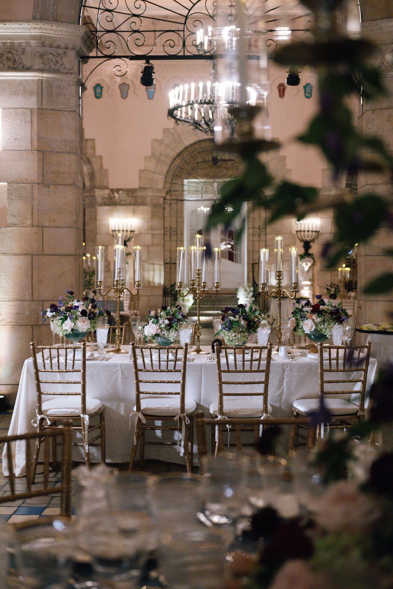 Romantic reception setup with gold chiavari chairs and white tablecloths in a historic stone venue.