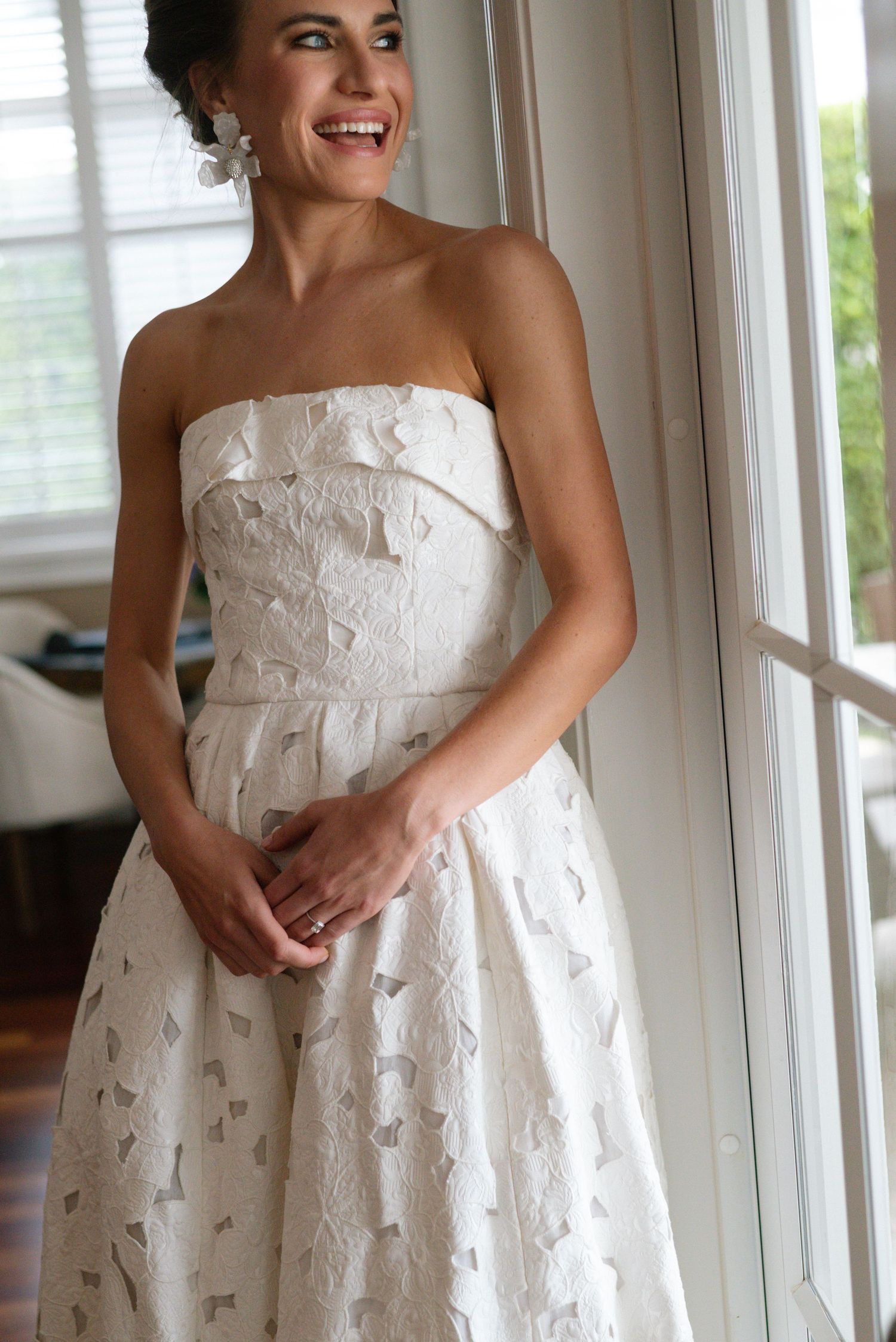 Elegant white textured wedding dress with strapless neckline by a window.
