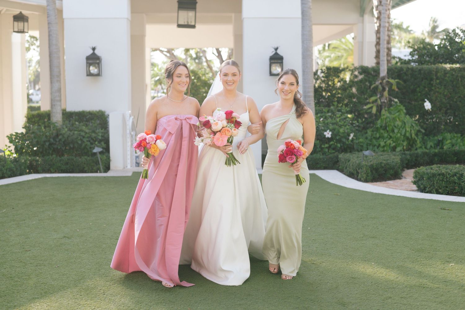 Wedding party in pink and white dresses posing together in front of a columned building.