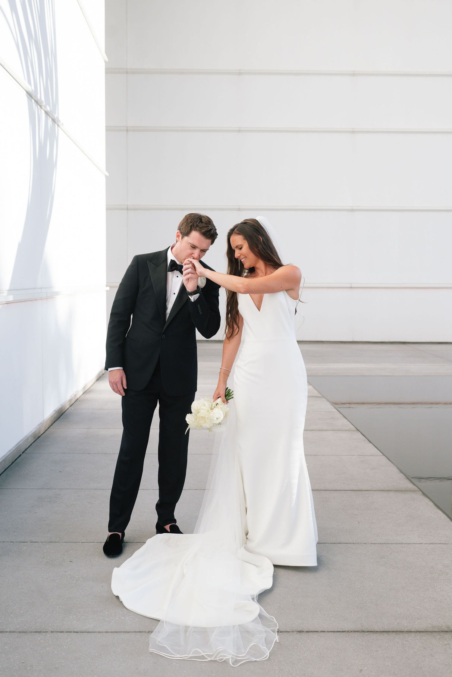A playful wedding moment captured in a bright white modern space with clean architectural lines.