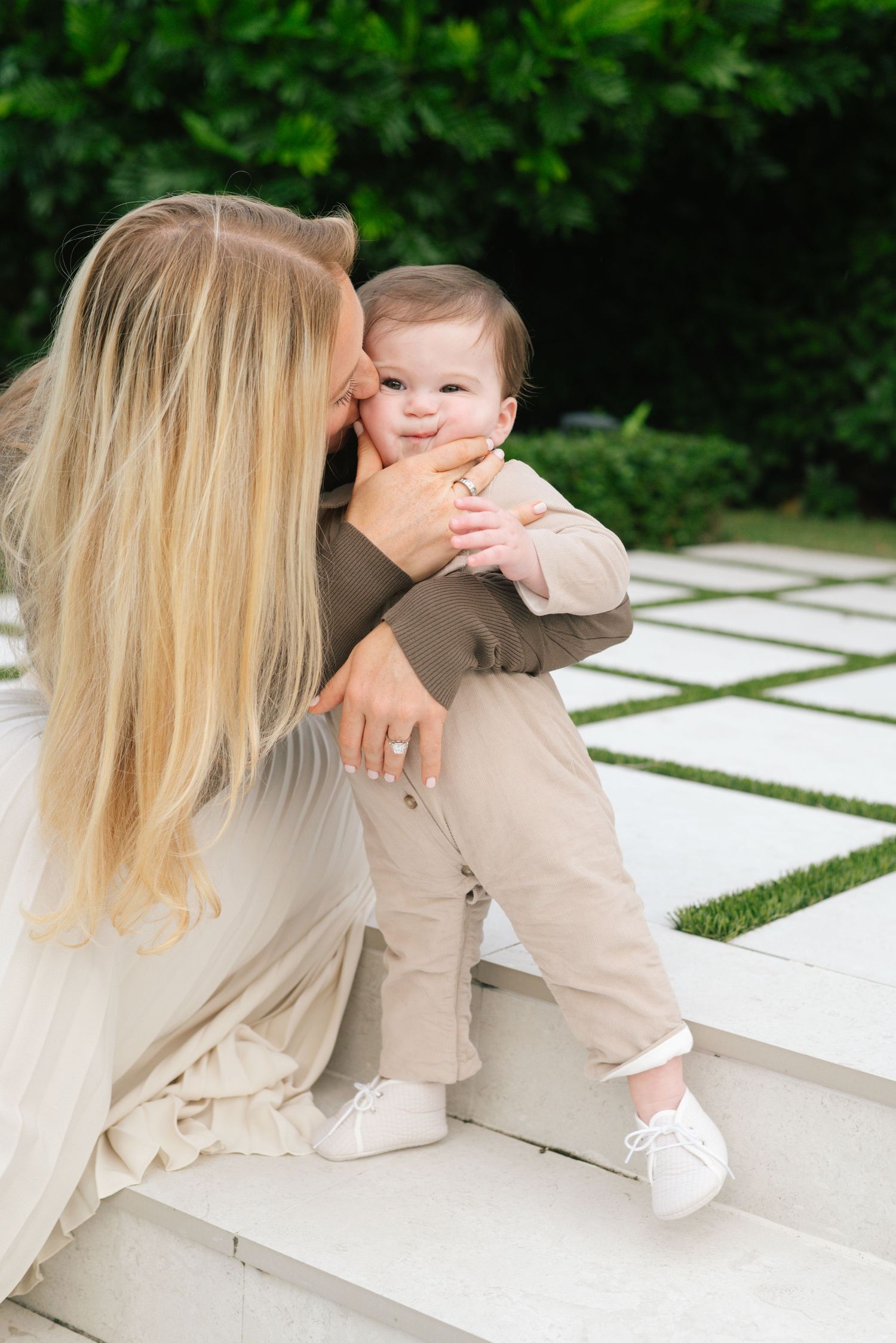 A tender moment shared between parent and baby wearing matching neutral tones on outdoor steps with greenery in background.