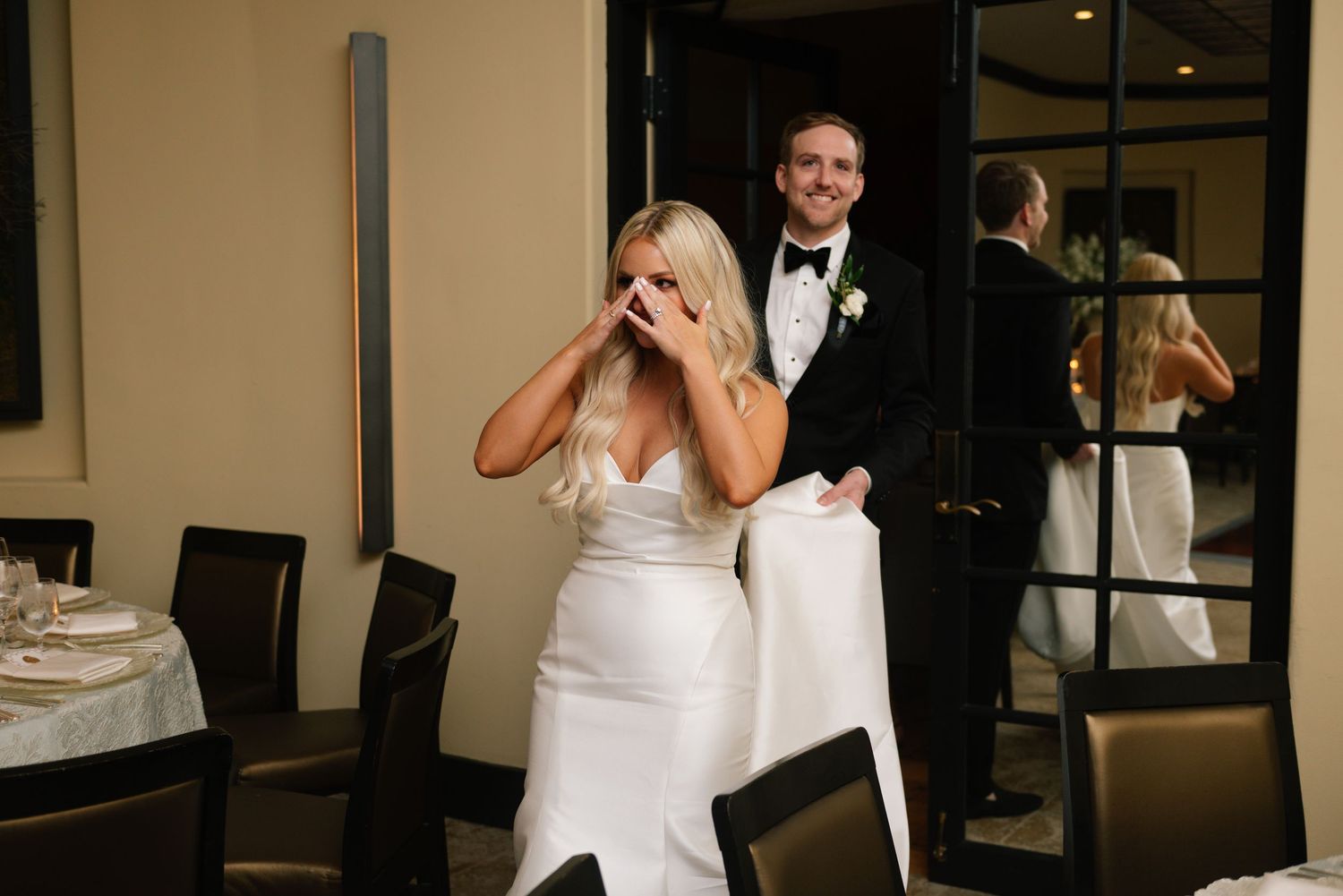 A couple shares an emotional moment during their wedding reception with reflections in a mirror behind them.