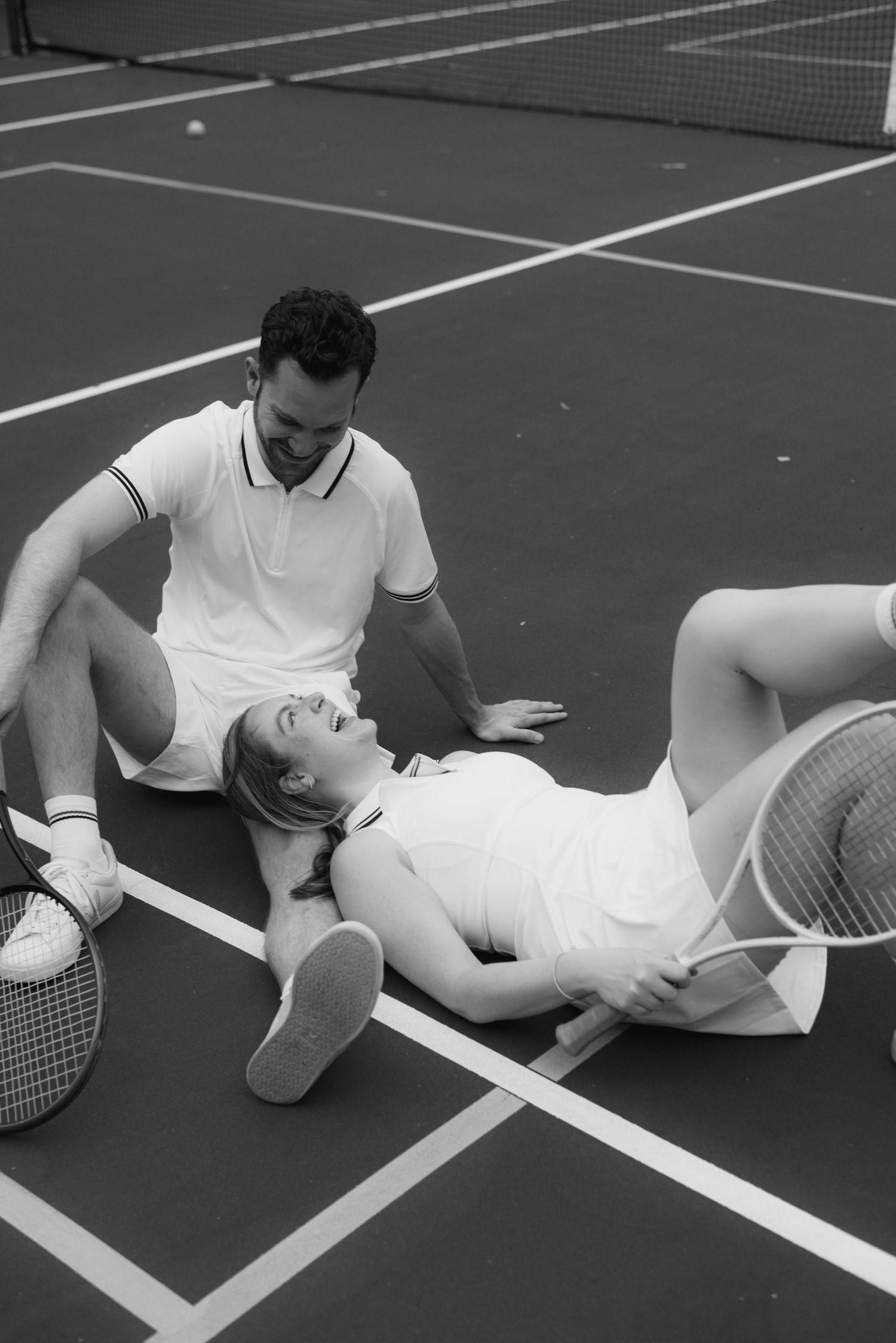 A black and white photo of two tennis players resting on the court after a match.