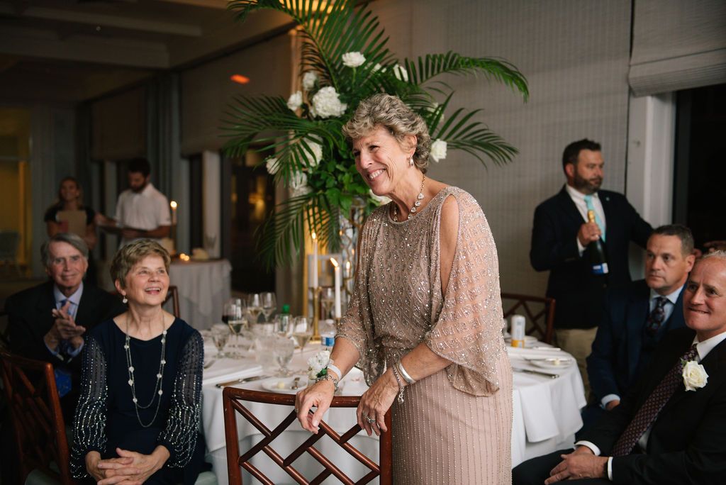 Wedding guest delivers speech during elegant reception with palm decor and candlelit tables.