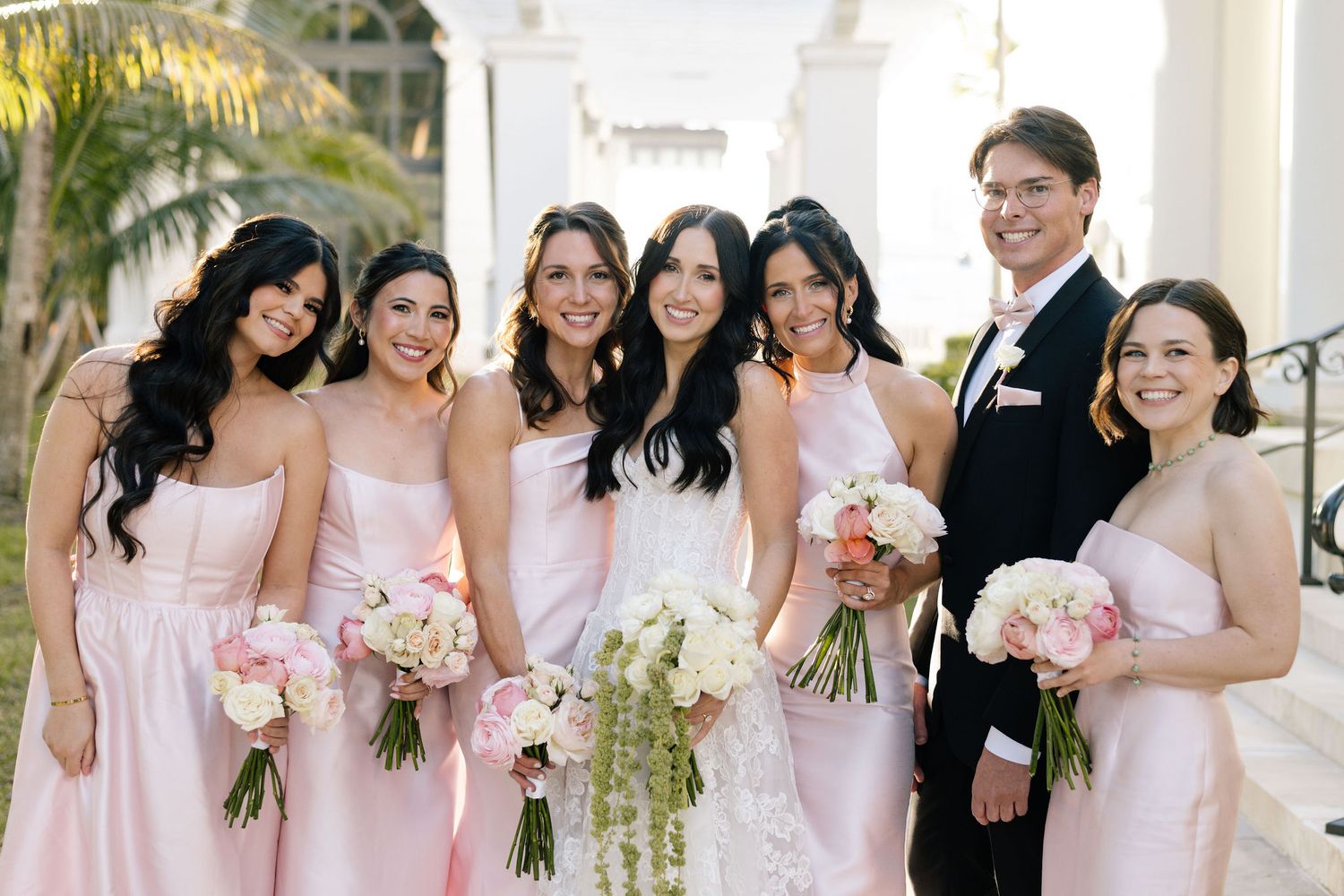 Bridesmaids in soft pink dresses pose with bouquets at an elegant wedding ceremony.