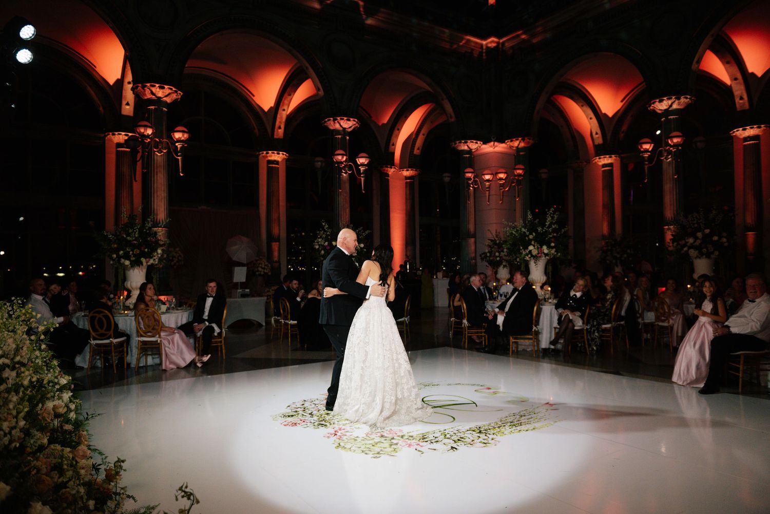 Wedding reception dance floor illuminated with dramatic red lighting and floral decorations.