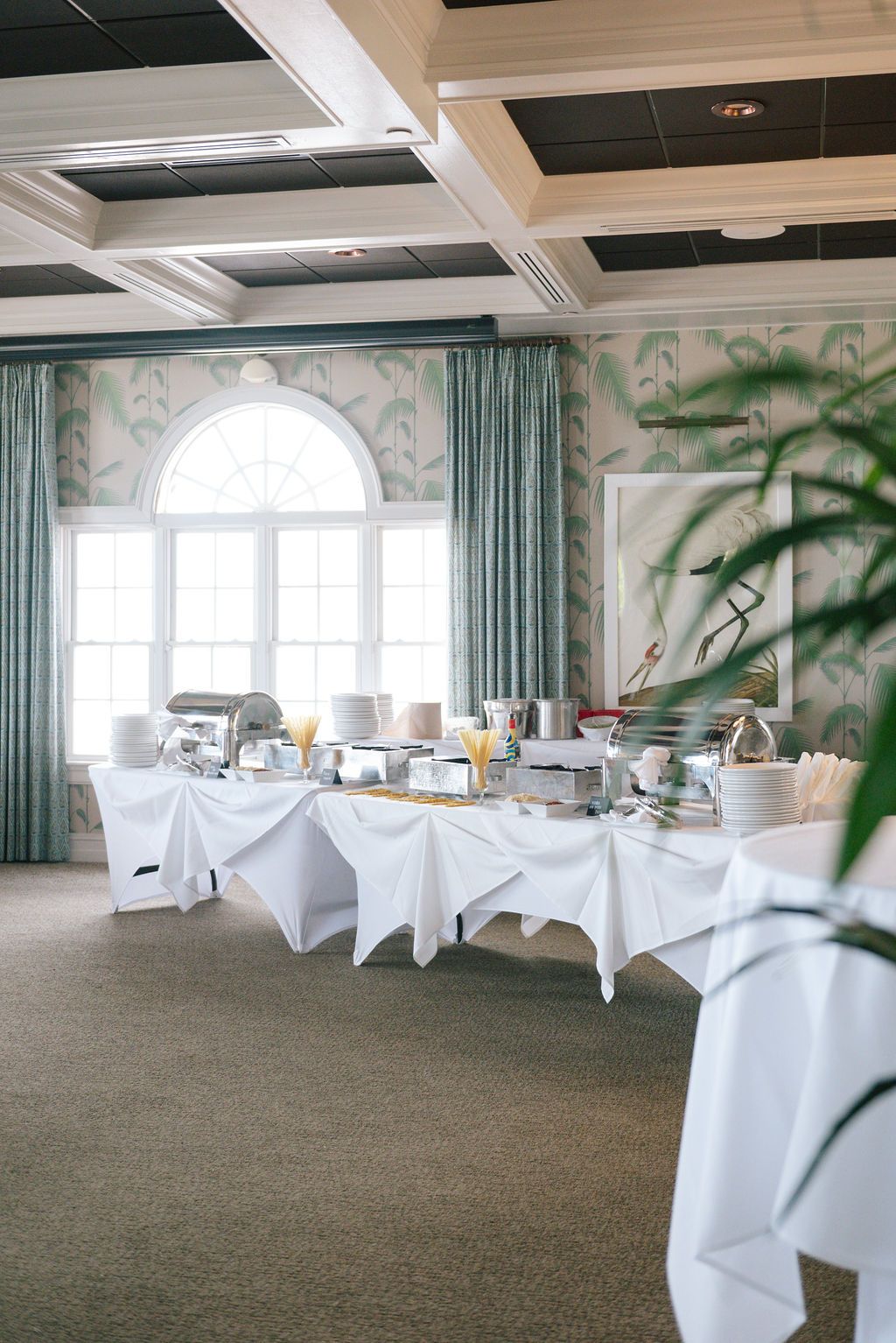 Elegant banquet hall setup with white chair covers and seafoam green curtains in a bright, airy space.