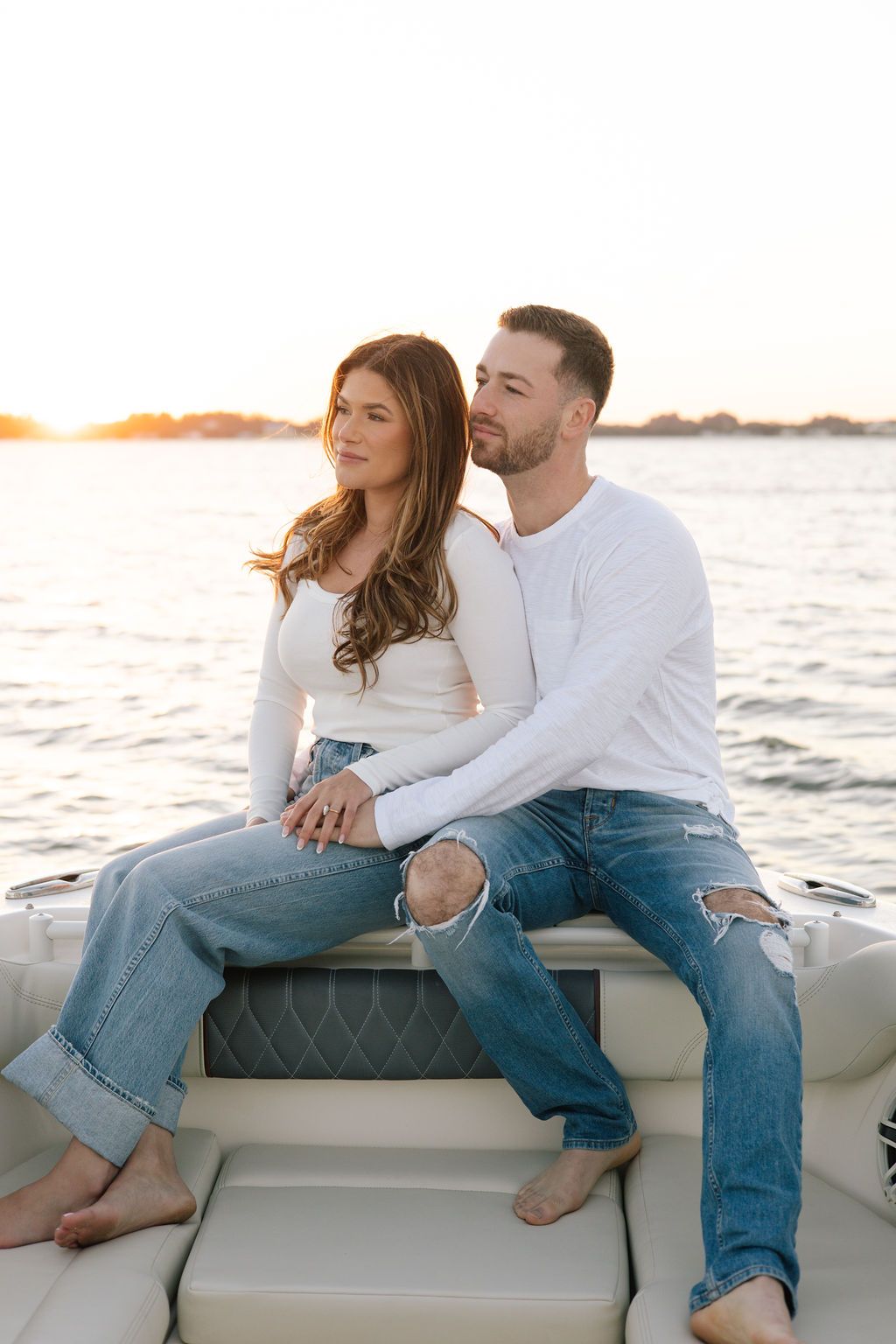 Couple relaxing on boat cushions during sunset cruise wearing matching white and denim.
