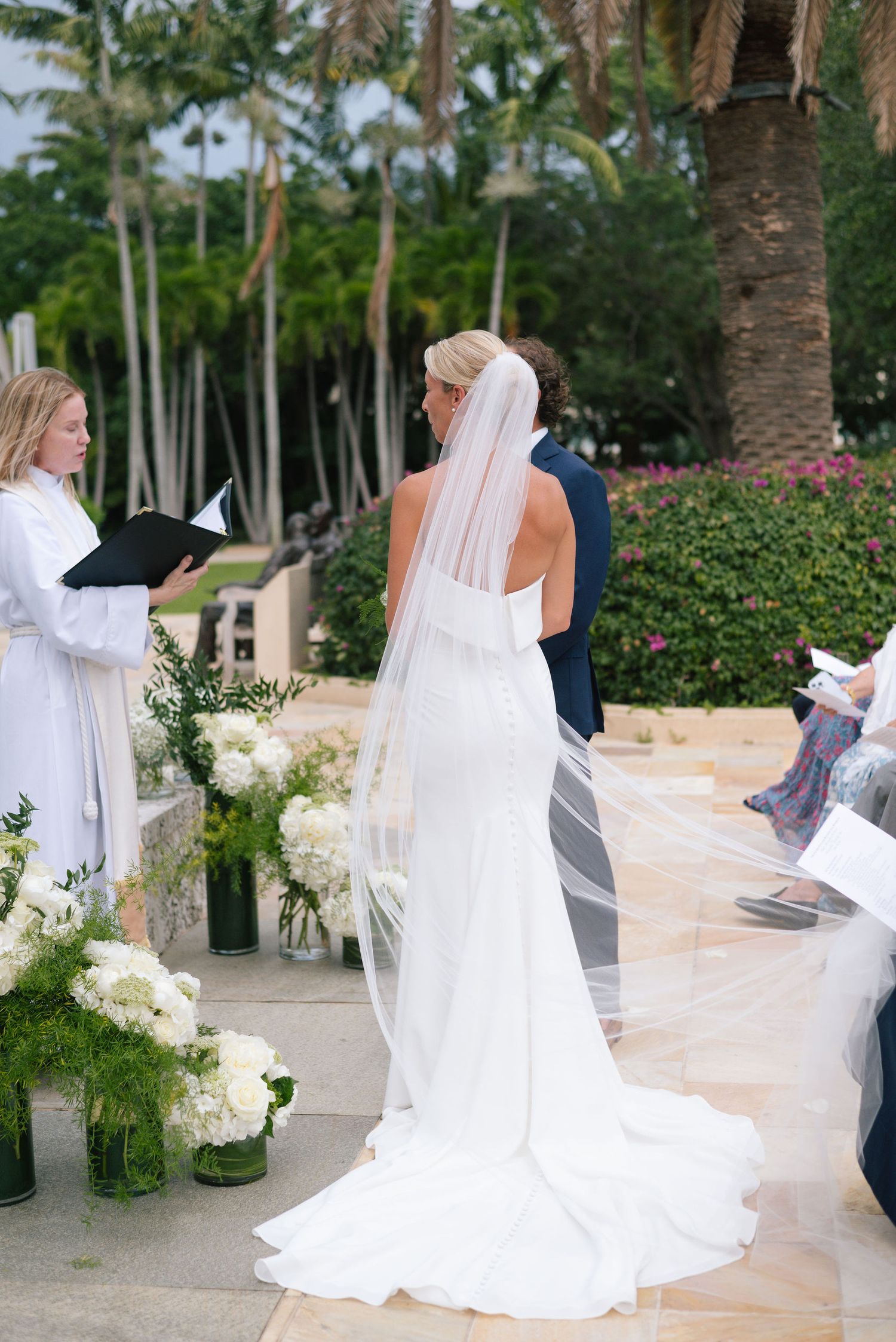 Flowing white wedding dress and veil details during an outdoor ceremony.