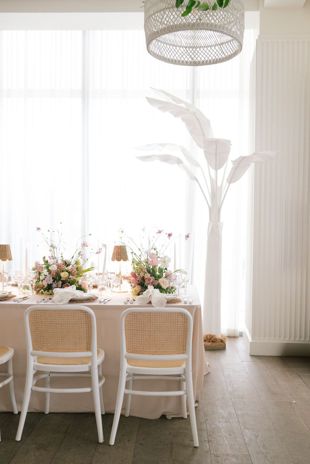 Bright reception space with white chairs, rattan pendant lights, and floral table arrangements.