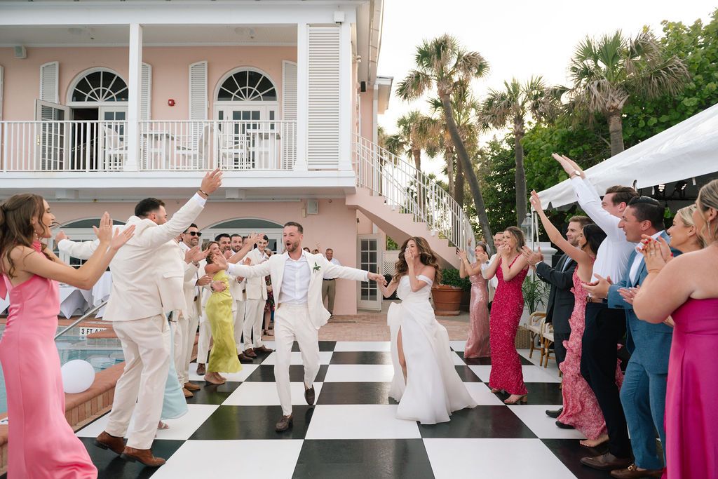 Wedding party dancing and celebrating on a black and white checkered floor at an outdoor venue.