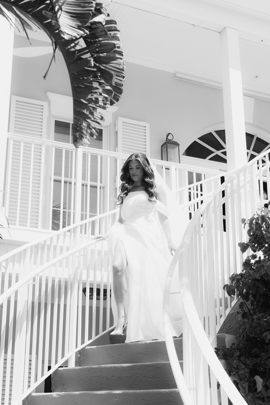 A flowing white wedding dress train cascades down elegant white stairs at a grand entrance.