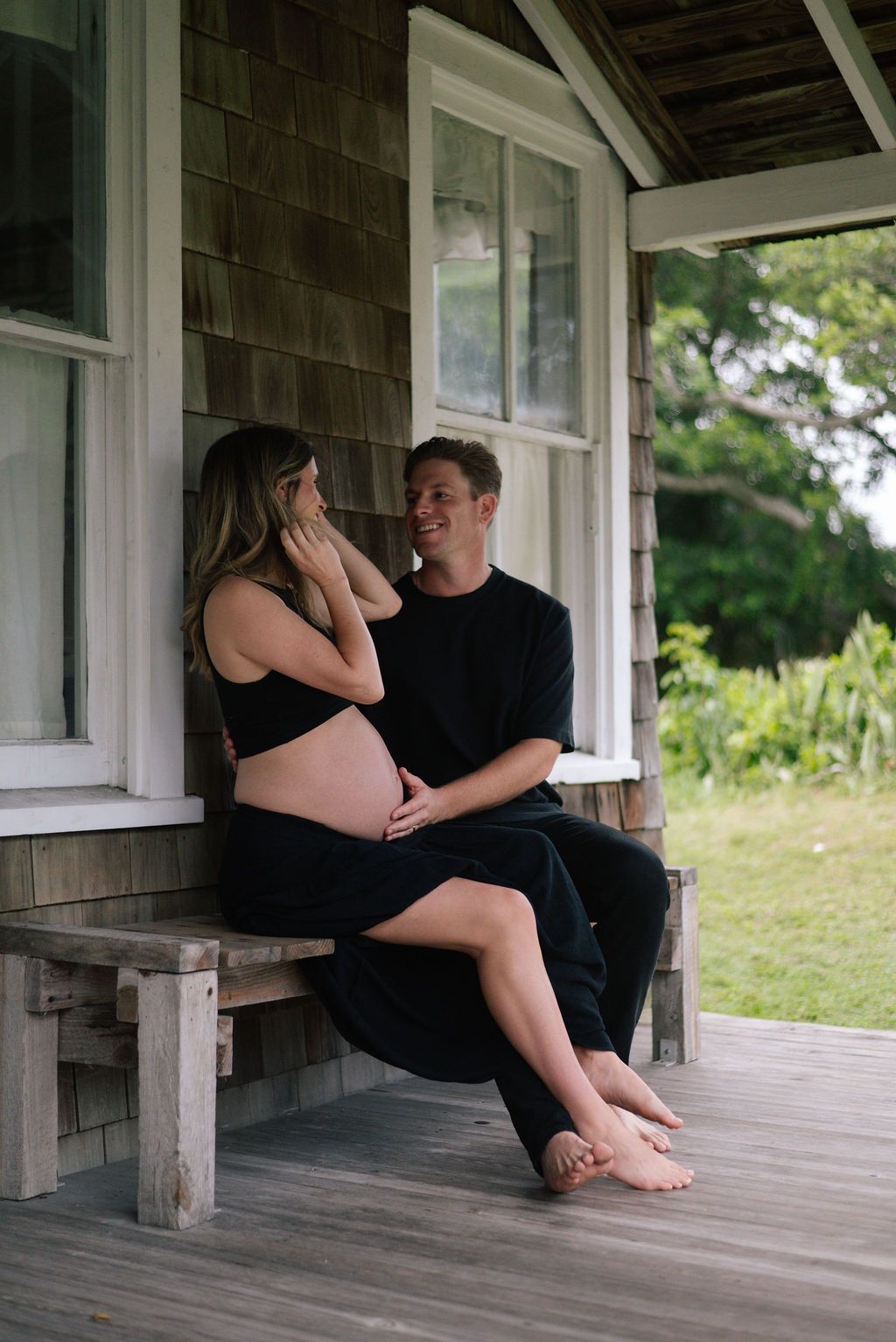 Couple shares romantic moments on a rustic porch during maternity photoshoot.