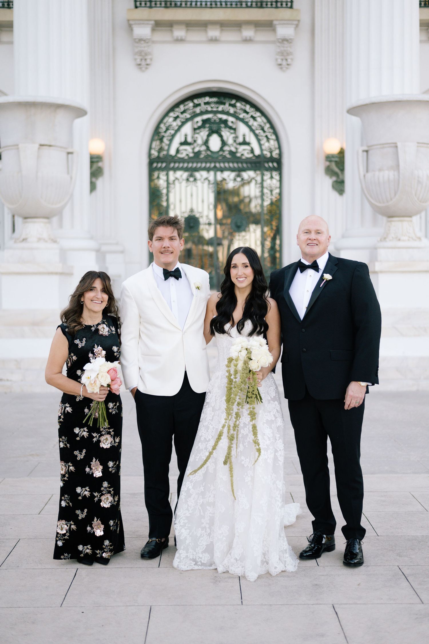 Wedding party poses in formal attire against white columned architecture.