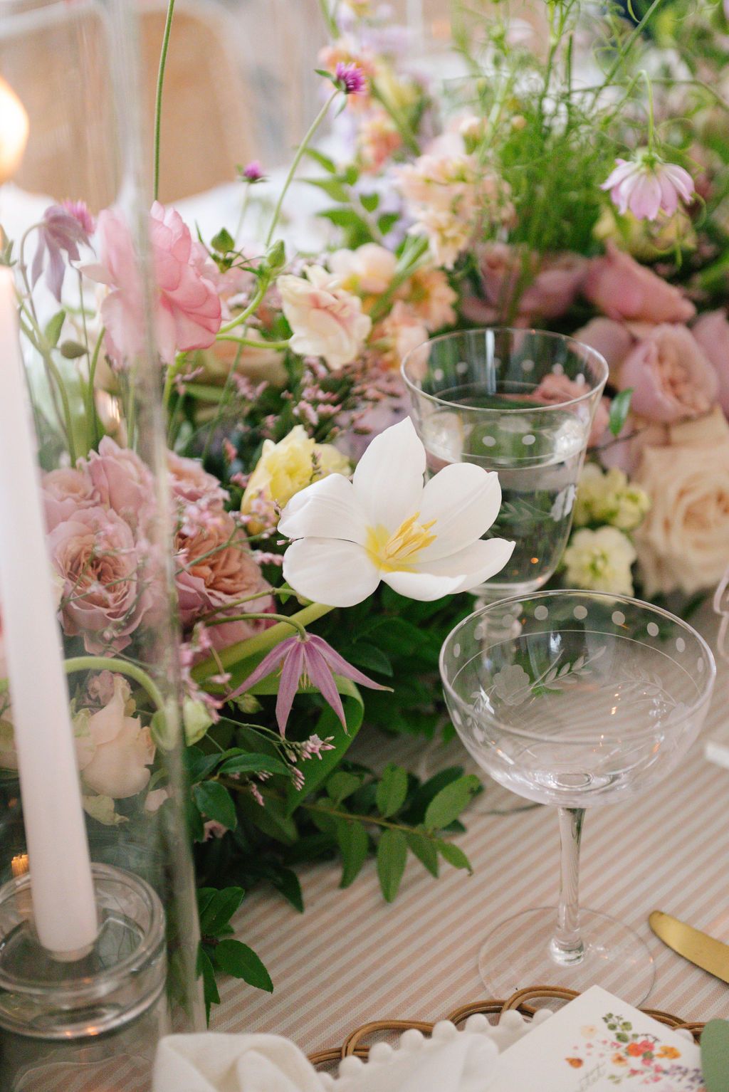 Romantic table setting with pink floral arrangements, white candles, and crystal glassware.