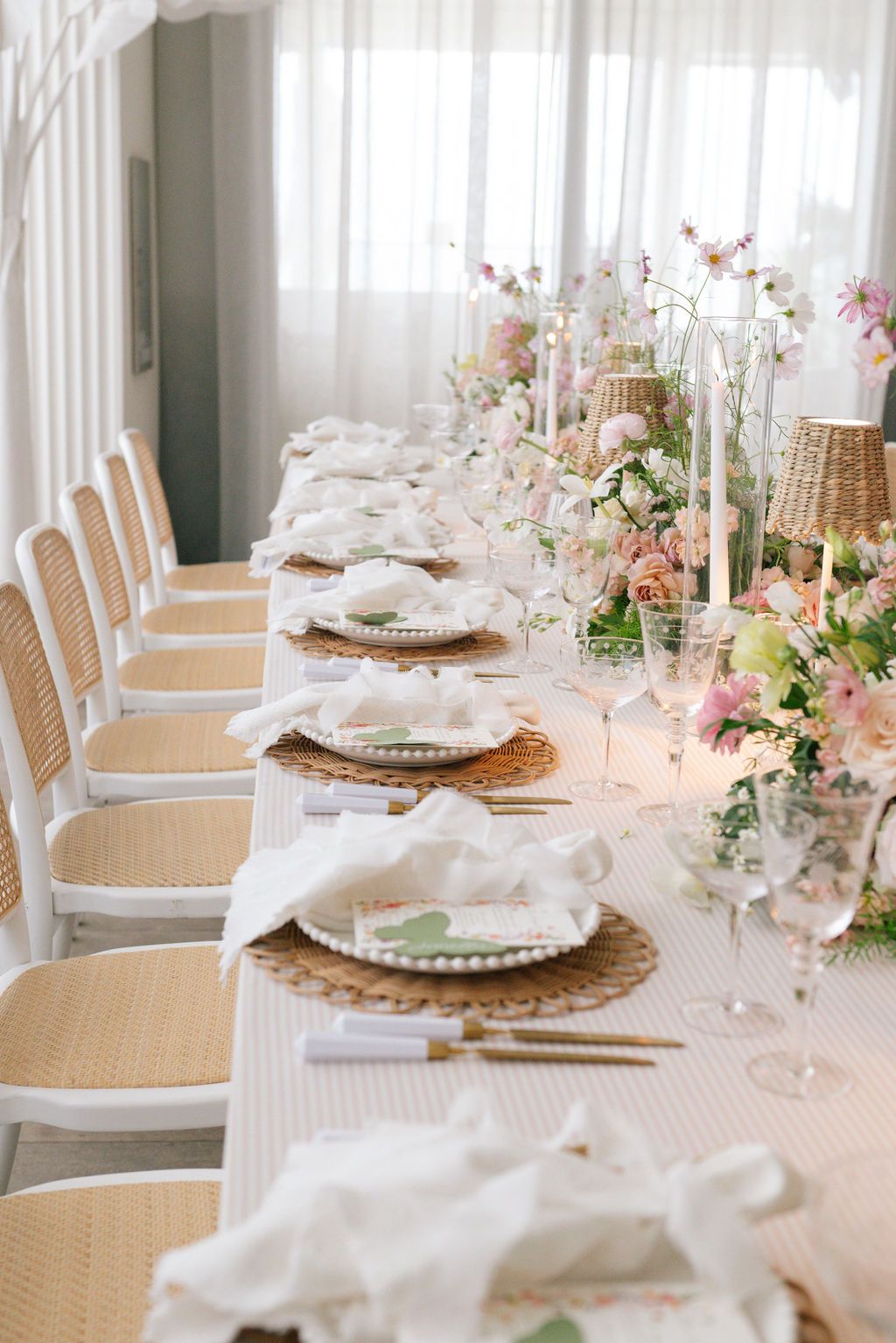 Long dining table with white chairs and romantic spring floral arrangements.
