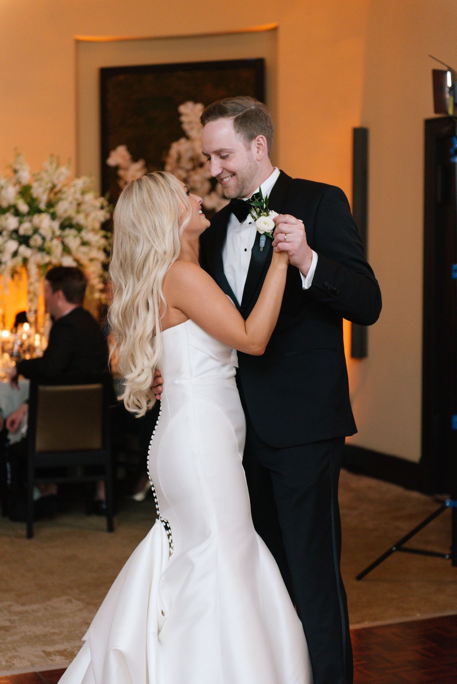 A couple shares an intimate dance moment at their wedding reception with elegant floral arrangements in the background.