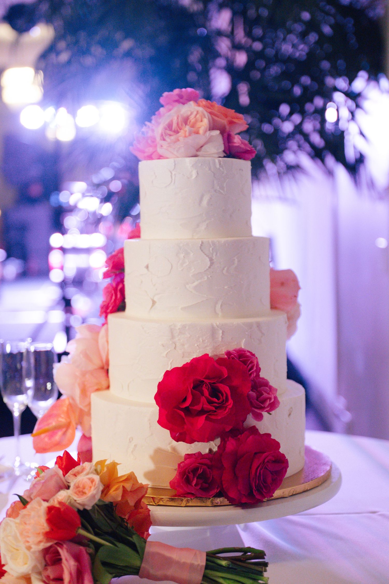 A collection of elegant white wedding cakes decorated with pink and red roses in romantic purple lighting.