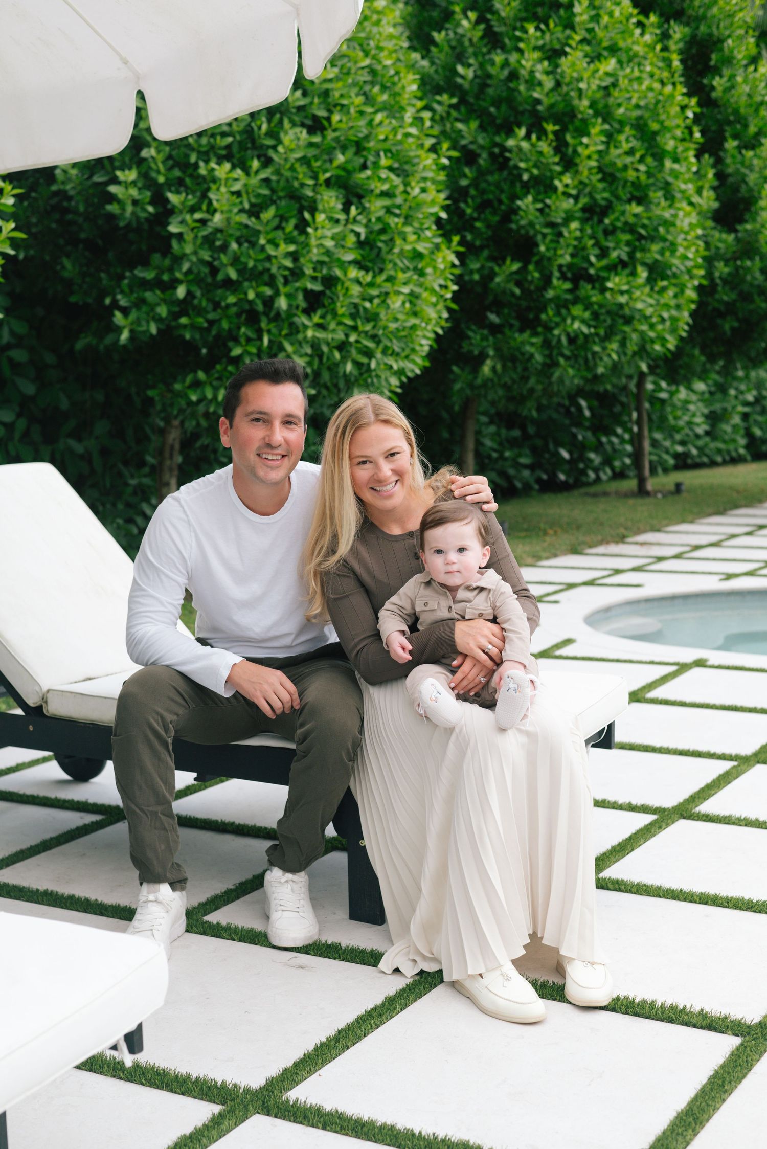 A family sits together on white outdoor furniture surrounded by green landscaping and modern patio design elements.