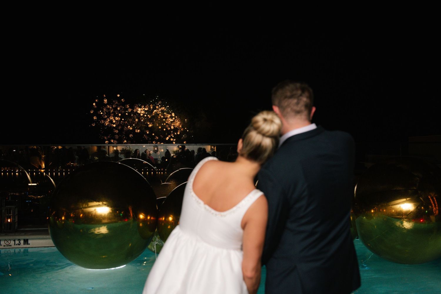 Romantic evening celebration by an illuminated pool with string lights overhead.