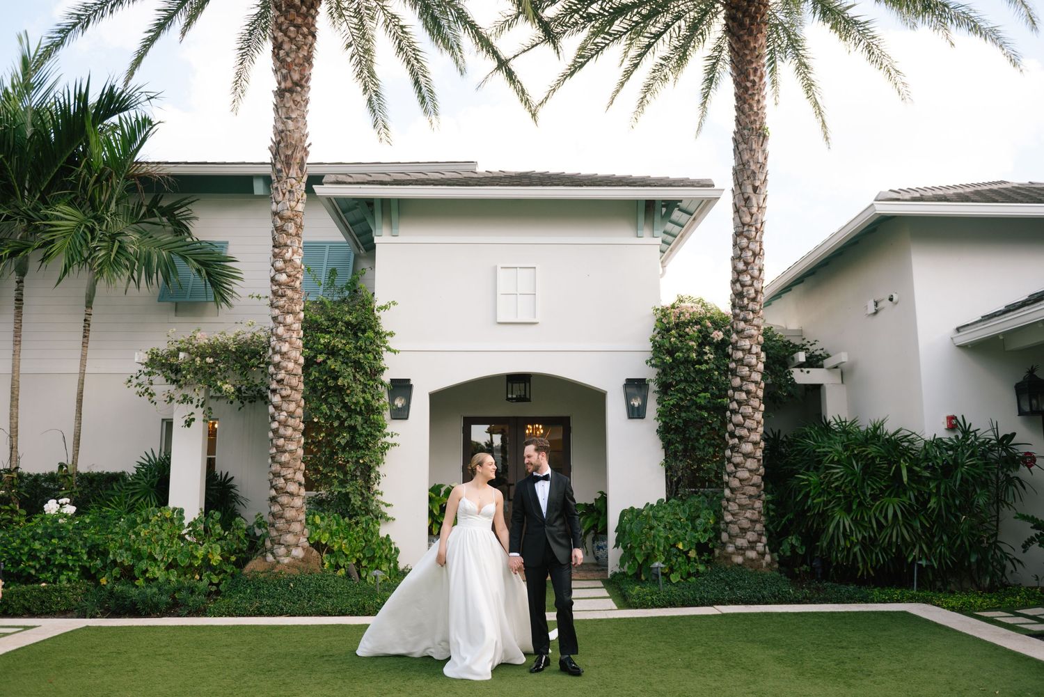A row of palm trees line a white building exterior creating a tropical wedding venue atmosphere.