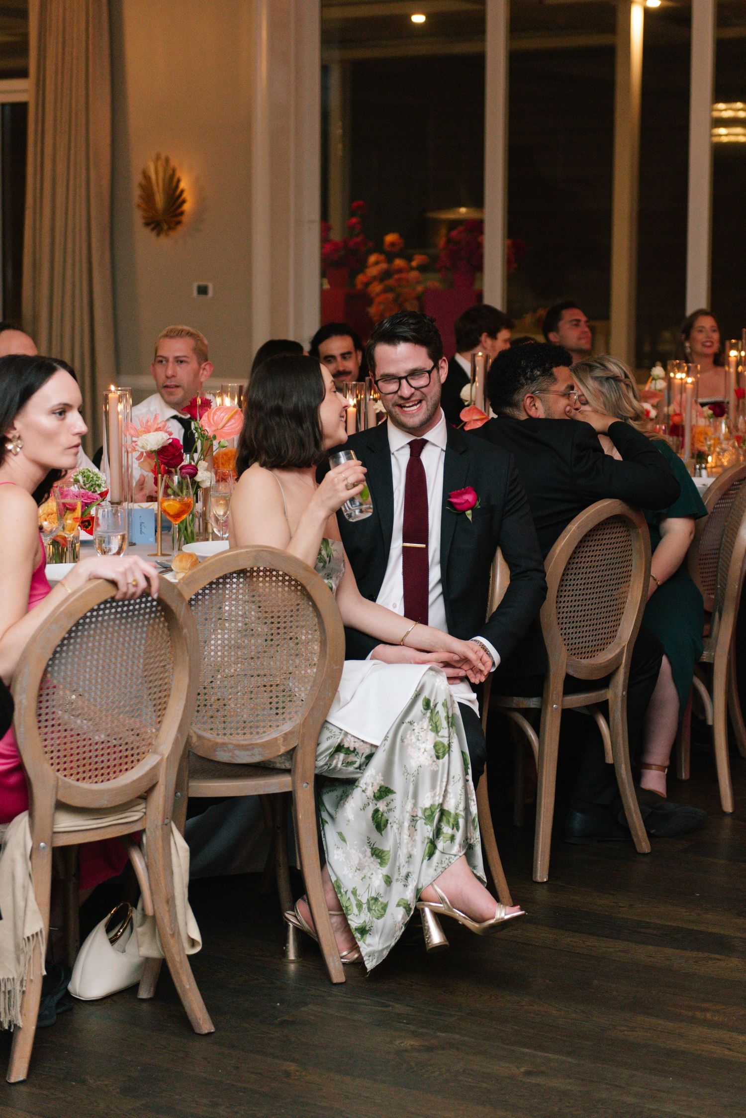 Wedding reception guests seated at elegant tables with cane-back chairs enjoying conversation.