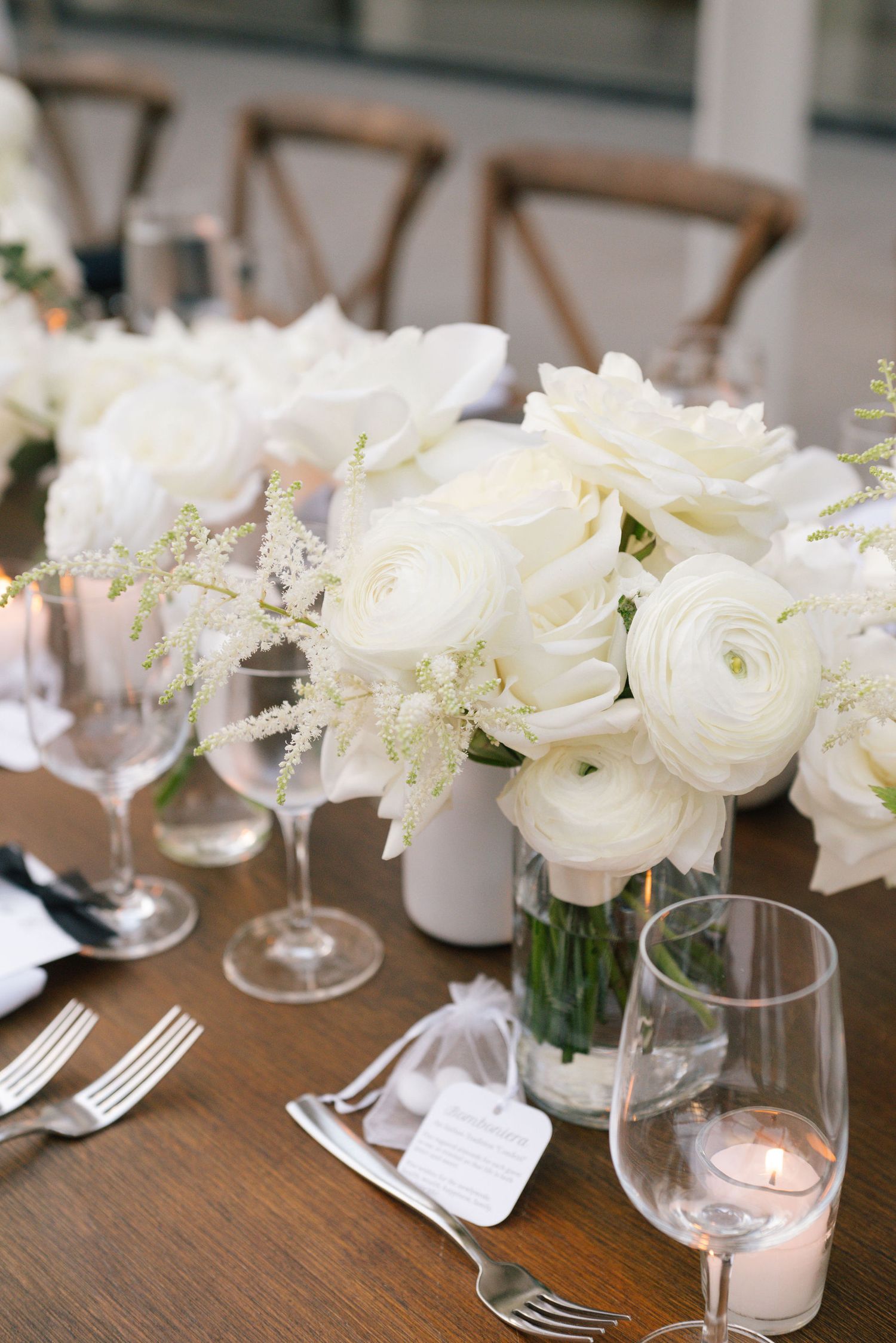 White floral centerpieces with candles and place settings on a rustic wooden table at an elegant wedding reception.