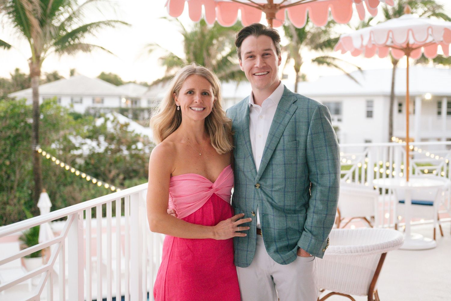 Wedding reception venue decorated with pink umbrellas and palm trees by the beach.
