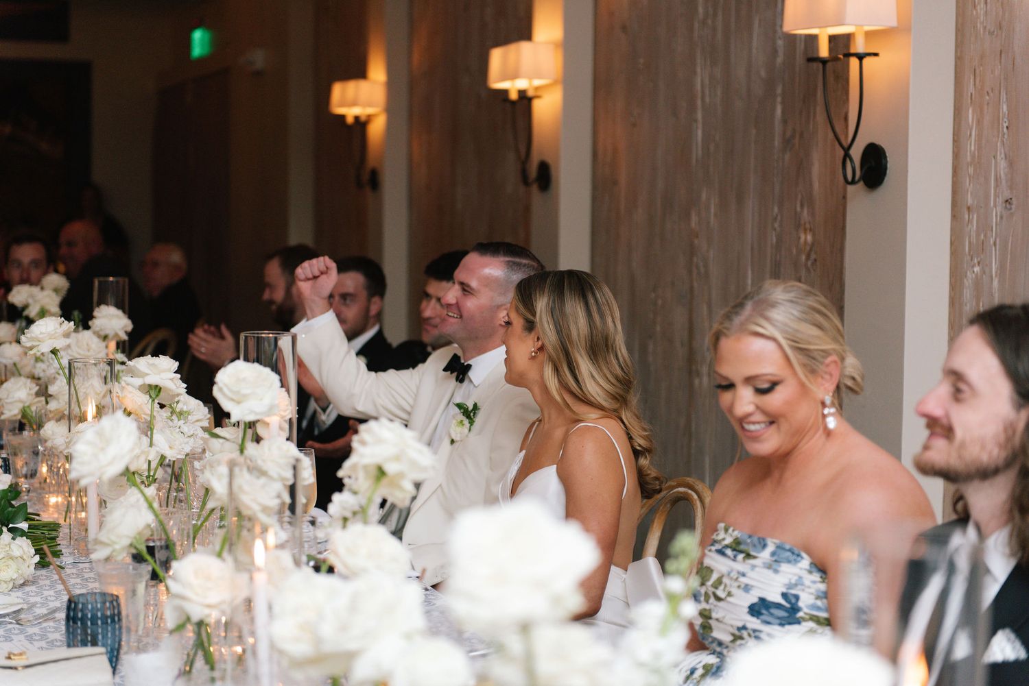 Elegant wedding reception with rustic wood walls, warm lighting and white floral centerpieces.