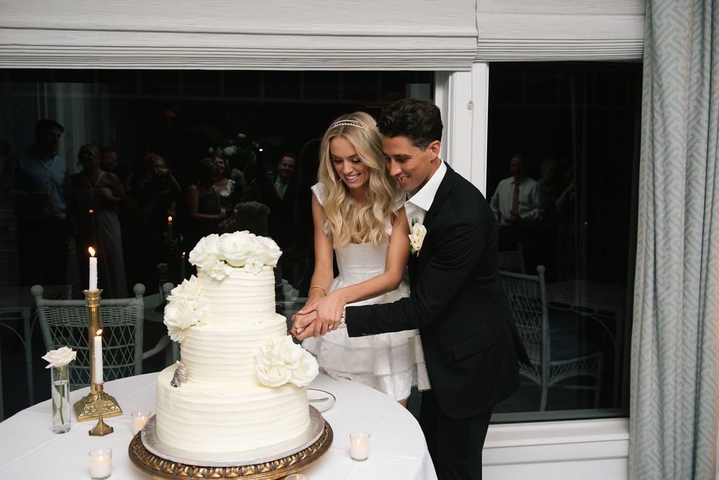 A white tiered wedding cake decorated with flowers sits on display at an elegant reception.