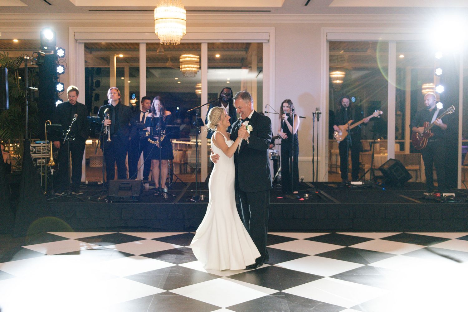 Wedding celebration on a black and white checkered dance floor with ambient lighting.