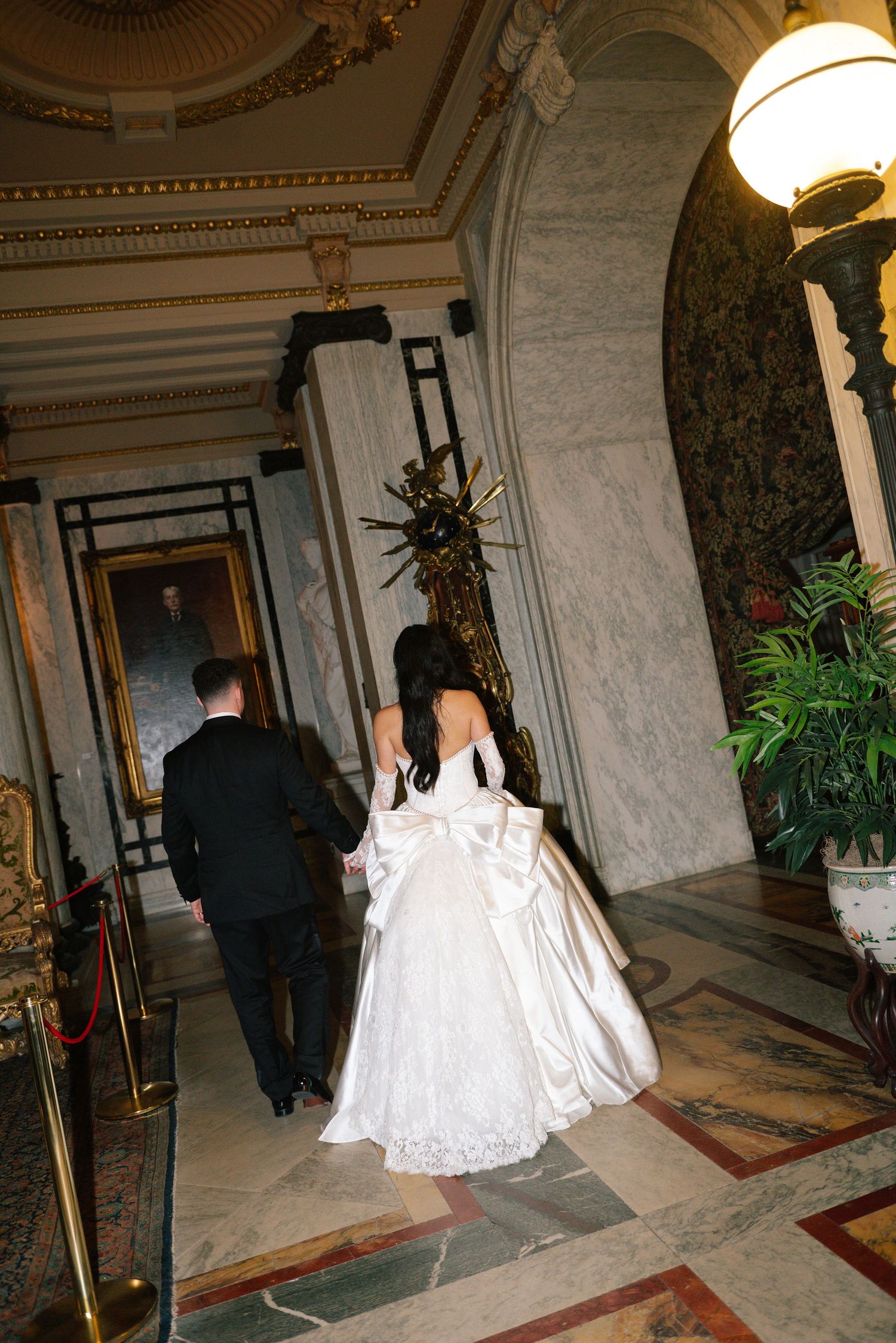 A couple walks through a luxurious marble hallway with ornate decor.